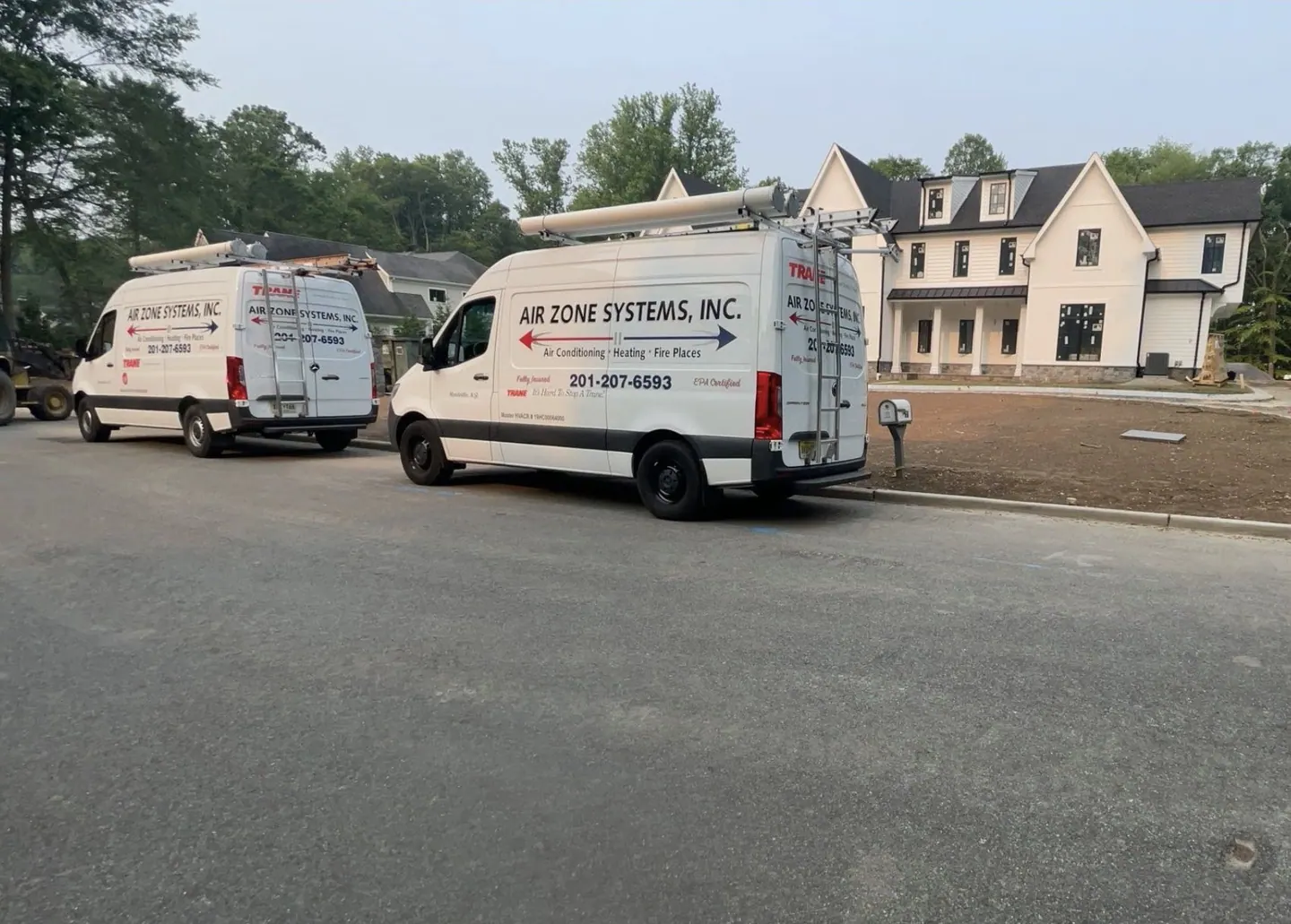 Two white Air Zone Systems, Inc. vans parked on a new street in front of a large new house with bare ground in front of it.