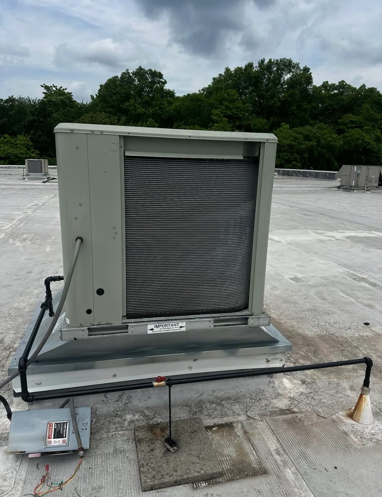 A gray-green condenser unit with an exposed coil on a roof curb, with gas piping and a disconnect box on a flat roof.